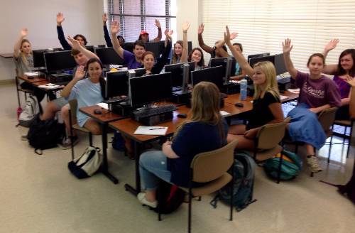 Students in a classroom raising their hands. 