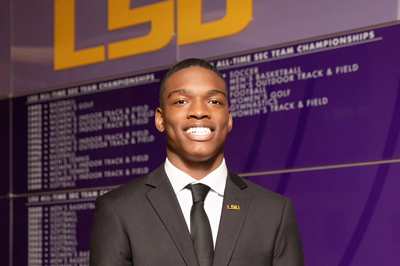 Zyan Williams wears a dark suit and smiles warmly as he stands in front of a branded wall, the LSU logo appears over his head.