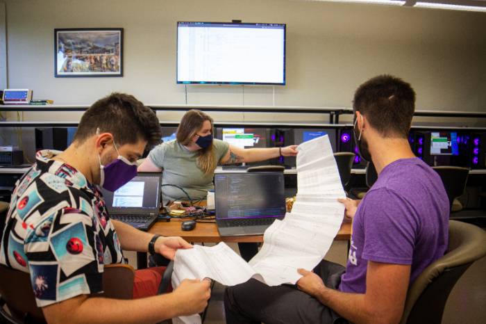 Three students holding a long sheet of paper in a computer lab